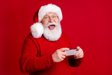 Photo of amazed crazy old man in santa claus headwear use smartphone enjoy x-mas magic miracle discounts wear sweater jumper isolated over bright shine color background