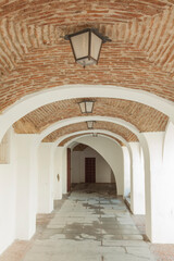 a portico in a Spanish town, with a brick vault ceiling and old lamps
