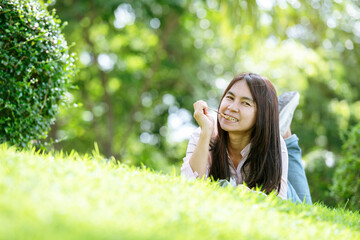 Naklejka na ściany i meble Relax beautiful asian woman smiling face Lying down on green grass field in outdoors garden park enjoy nature morning. Freedom Lifestyle woman breathing fresh air in green park on spring lawn outdoors