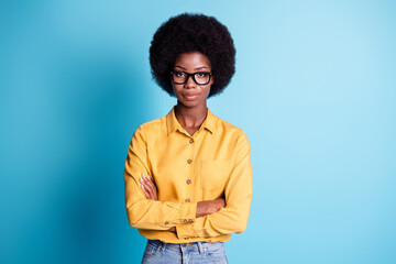 Fototapeta na wymiar Photo of dark skin big volume hairstyle lady crossed hands confident self-assured look bossy manager prepare make report wear eyeglasses jeans yellow shirt isolated blue color background