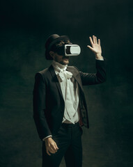 Playing VR. Young man in suit as Dorian Gray isolated on dark green background. Retro style, comparison of eras concept. Beautiful male model like classic literature character, old-fashioned.