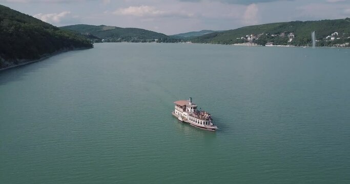 Panoramic round aerial video shooting from a drone retro ship with passengers floating on the lake against the background of mountains and forests
