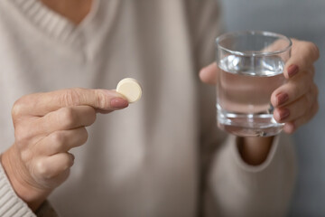 Elderly female hands hold pill and glass of water close up. Drugs for seniors people, brain and nervous system treatment, old woman take herbal sedative. Senile diseases prevention, healthcare concept