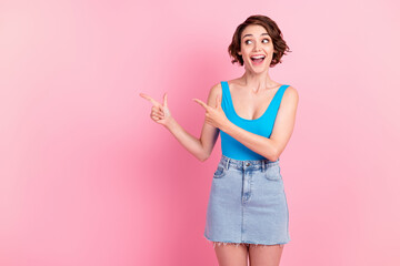 Photo of cute charming young lady directing fingers excited look empty space demonstrate discount regular costumer wear denim mini skirt blue singlet isolated pink color background