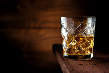 Half a glass of whiskey with ice cubes on an old wooden table, rustic style