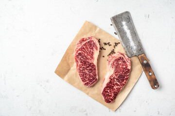 Two raw marble beef steaks on craft paper and a meat cleaver, top view and copy space