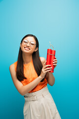 happy asian girl in glasses holding dynamite sticks on blue