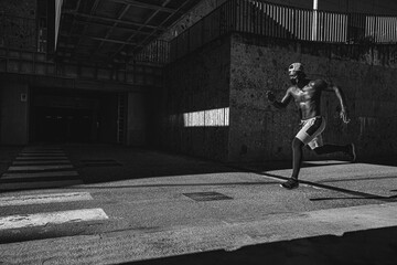 Athletic black man is training in front of the grey wall while wearing a mask. Black and white photo.