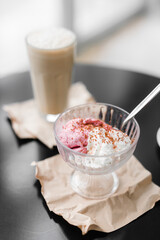ice cream white and pink in a transparent cream bowl on a black table against the background of coffee