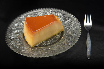 Milk pudding on a plate on black table with black background, selective focus