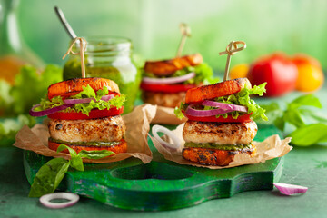 Delicious roasted pumpkin turkey burger with tomatoes and pesto on green wooden board.