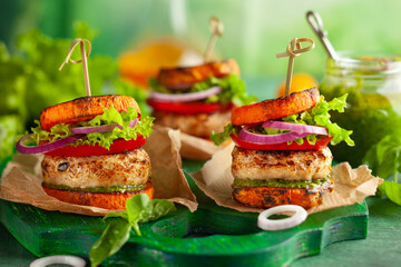Delicious roasted pumpkin turkey burger with tomatoes and pesto on green wooden board.