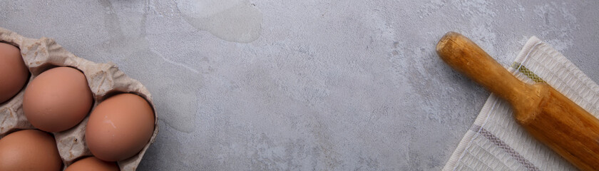 Part of a tray with eggs rolling pin and kitchen towel on a gray background.
