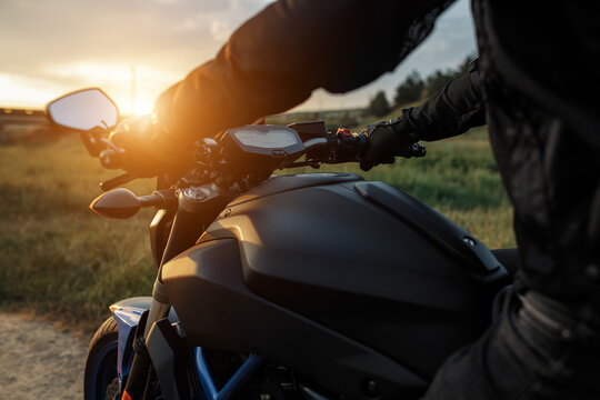 Close-up photo of biker sitting on motorcycle in sunset on the country road. © Screaghin