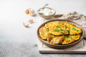 Green zucchini fritters, vegetarian zucchini pancakes with fresh herbs and garlic, served with cream sauce on white background, selective focus