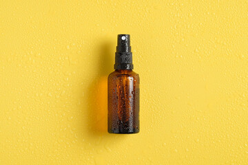 Wet amber glass spray bottle mockup with water drops on yellow background, view from above. Suntan...