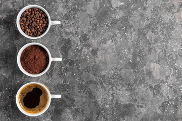 Coffee beans, ground coffee and espresso in cups on gray background