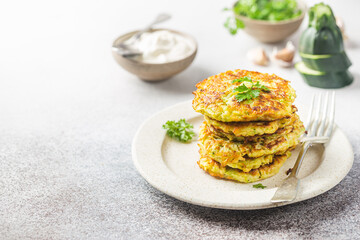 Green zucchini fritters, vegetarian zucchini pancakes with fresh herbs and garlic, served with cream sauce on white background, selective focus