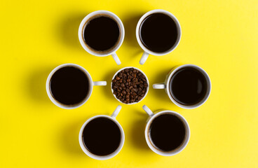 Cups of espresso coffee with coffee beans on yellow background