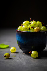 Fresh ripe berries of green gooseberry in a blue bowl on dark gray background. Selective focus.