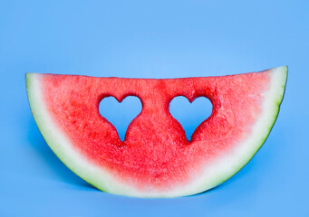 Obraz na płótnie Canvas A watermelon slice with hearts shape holes in it on blue background