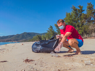 Fototapeta na wymiar Activist volunteer Man in medical face mask pick up garbage that pollute beach sand near sea. Problem of spilled rubbish trash caused by man-made, planet pollution and environmental protection concept