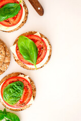 Crispbread with cheese, tomato and basil leaf on a light background top view. Tasty diet snack or breakfast. Vegetarian food.