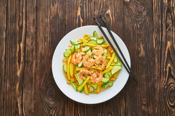 A spicy mango salad with vegetables, chili and shrimps, chopsticks on wooden background, asian food concept top view with copy space