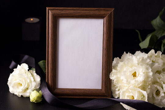 Wooden mourning photo frame next to white flowers on black background