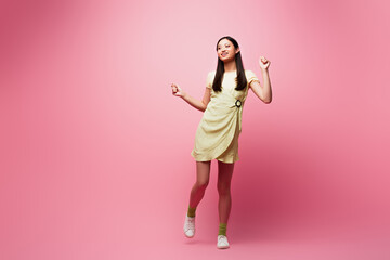 cheerful asian girl in dress dancing on pink