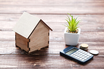 House model with coins and calculator on brown wooden table