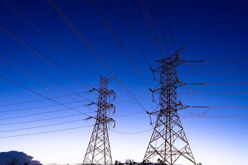 A High-voltage electricity transmission pylons against evening twilight sunset background.