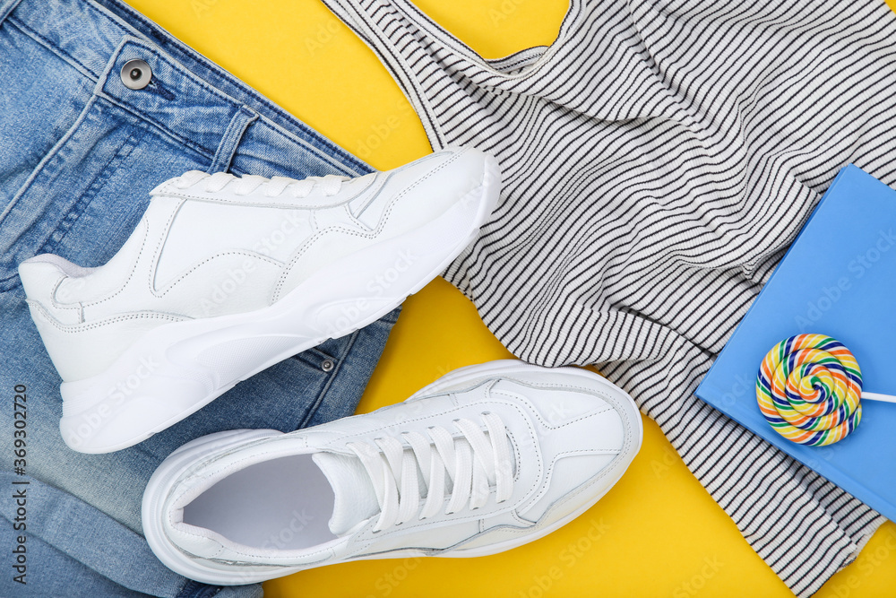 Wall mural Pair of white shoes with fashion clothing, notepad and lollipop on yellow background