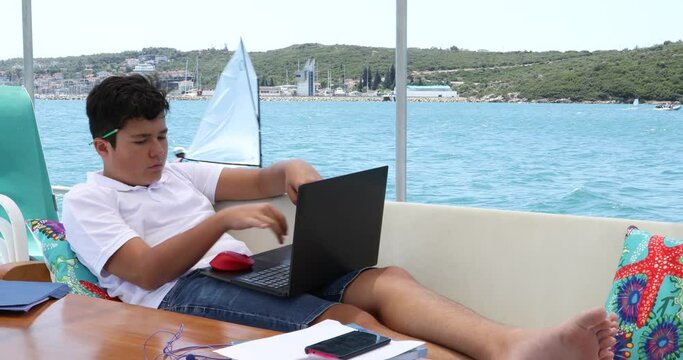 Teenage boy studying on yacht deck Online learning education distance learning for kids at home Homeschooling during quarantine or isolation