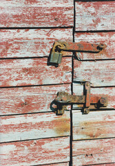Rugged red shed gate locked with rusty lock and fittings.
