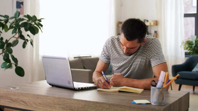 remote job, technology and people concept - young man with notebook and laptop computer working at home office