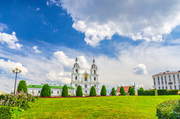 Fototapeta premium Holy Spirit Cathedral Orthodox Church Baroque style building and green grass lawn in Upper Town Minsk historical city centre, blue sky white clouds in sunny summer day, Republic of Belarus