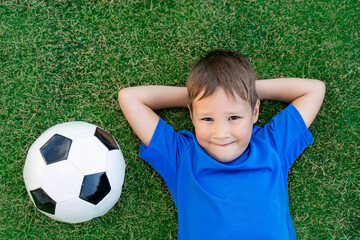 A little boy lies on a green soccer field, a soccer ball, top view.
