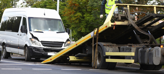 Wrecked minibus stands next to tow truck. Broken and wrecked car transportation services concept