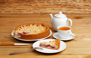 Homemade plum pie, cup of tea and teapot on wooden table.