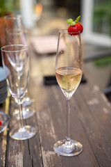 A glass with champagne and strawberries in the summer on a wooden table. Outdoor party.