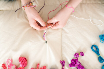 Close-up detail from above of a girl's hands making colored bracelets.