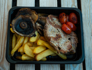 Grilled street food closeup mushrooms, french fries, grilled fish, potato. Served in a plate, selective focus on a wooden table, background.