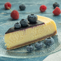 Blueberry and raspberry cheesecake, served on a transparent plate with brown sugar. Glass of milk on a light blue wooden background.