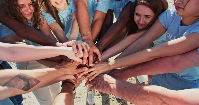 People of different ages and races are united to protect environment from pollution. Happy volunteers stacking hands together to cheer and boost team spirit. Friendship, teamwork, volunteering.
