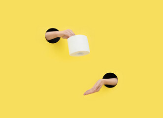 A female hand gives toilet paper on a yellow background. Hand in a paper hole. Help concept.