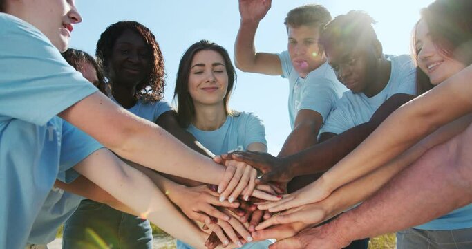 Enthusiastic team of volunteers cheering up, boosting team spirit. Friendly multiracial evironmentalists stacking hands before garbage collecting. Environmental conservation, biosphere protection.