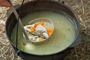 Fish soup is cooked on the fire. Ears in an iron bowl in nature.