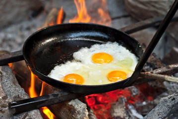 An omelet with three eggs is fried over a fire. Eggs are cooked in a pan on a hike.