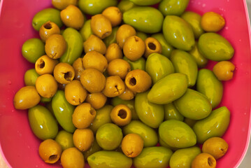 Yellow and green olives in a pink plate. Assorted olives close up.